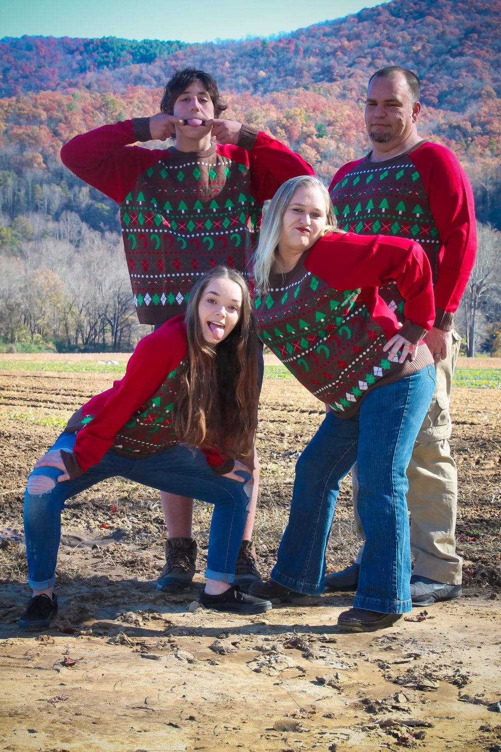 Family wearing matching Christmas sweaters poses playfully against autumn mountain backdrop.