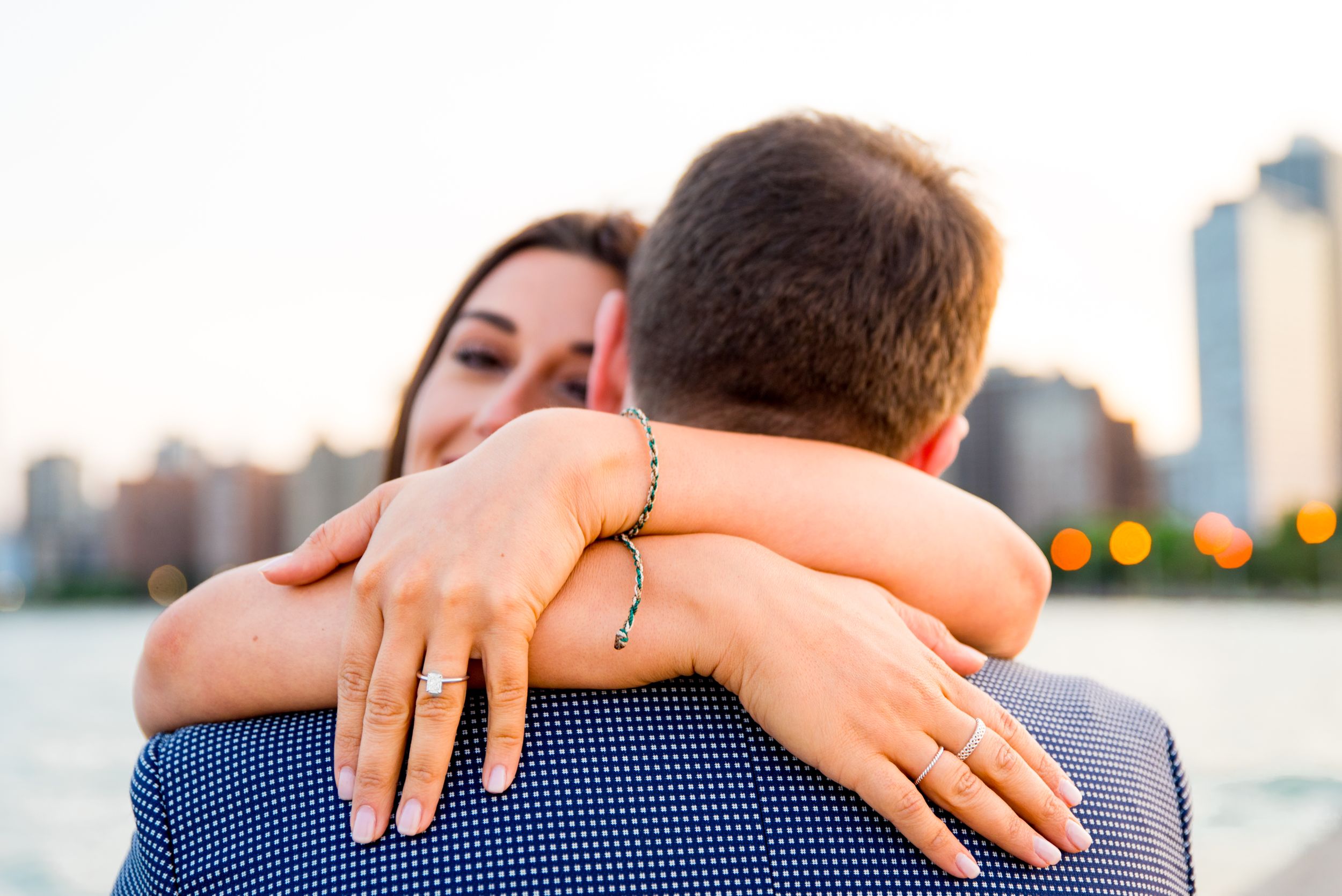 woman hugging new fiance showing off her ring and peeking over his shoulder