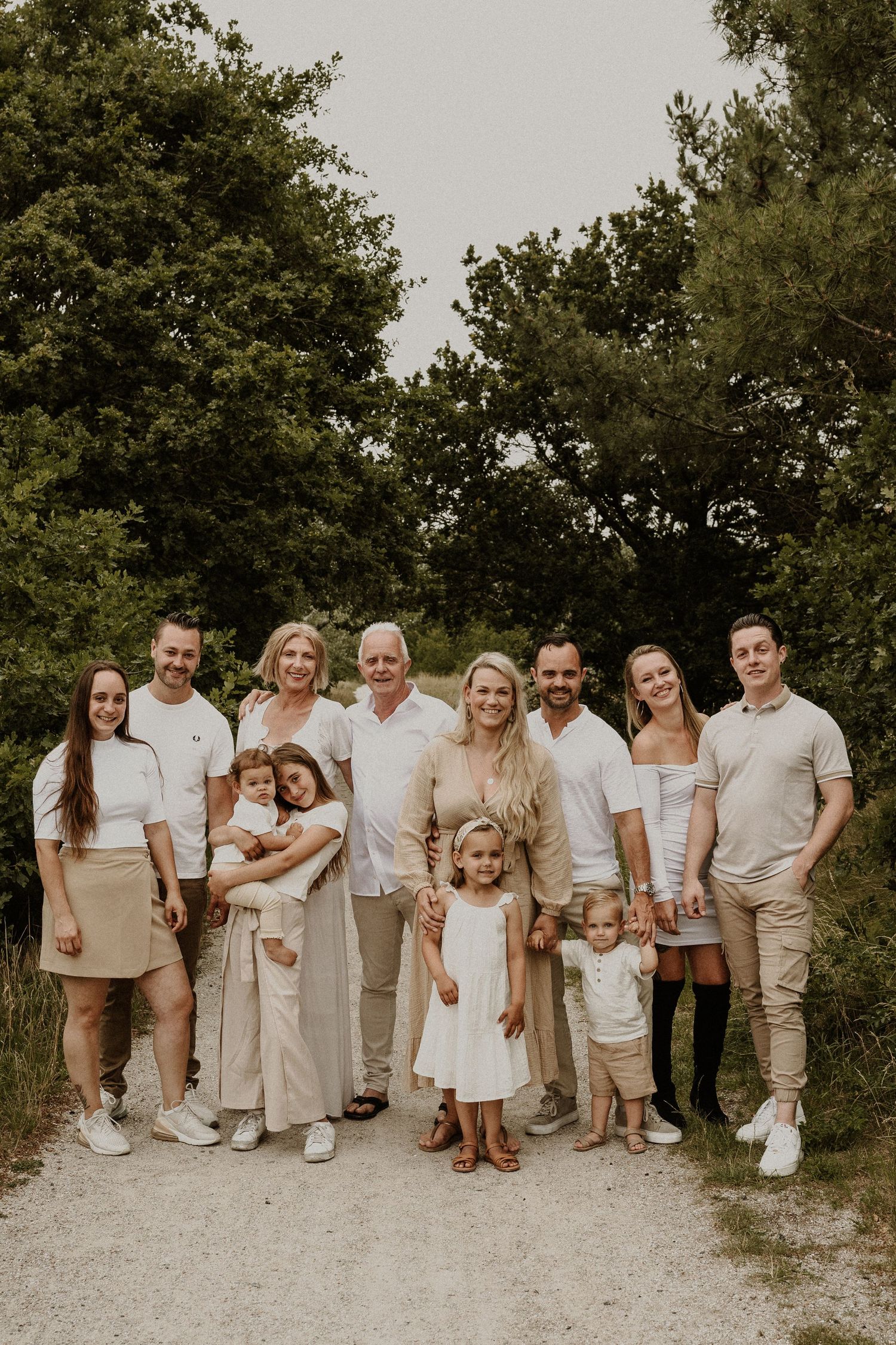 Family portrait of group wearing coordinated white and beige outfits on outdoor path.