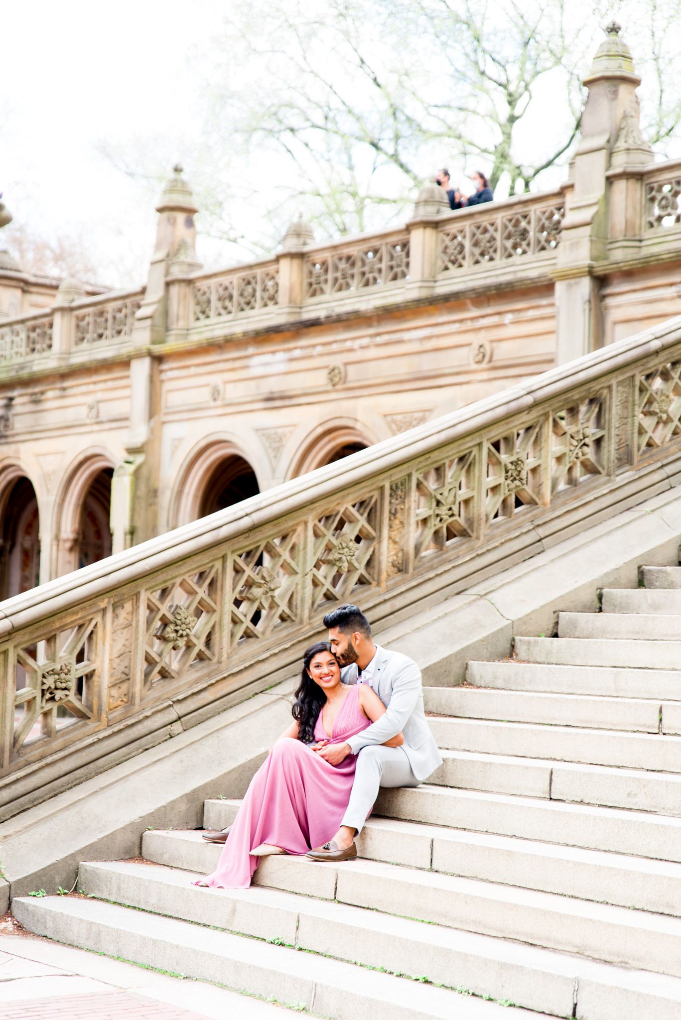 woman in pink dress and man in grey suit sitting on Bethesda Terrace steps and laughing with each other at Central Park