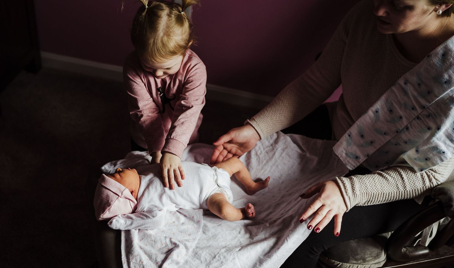 toddler touching her newborn sister in sudbury ma home
