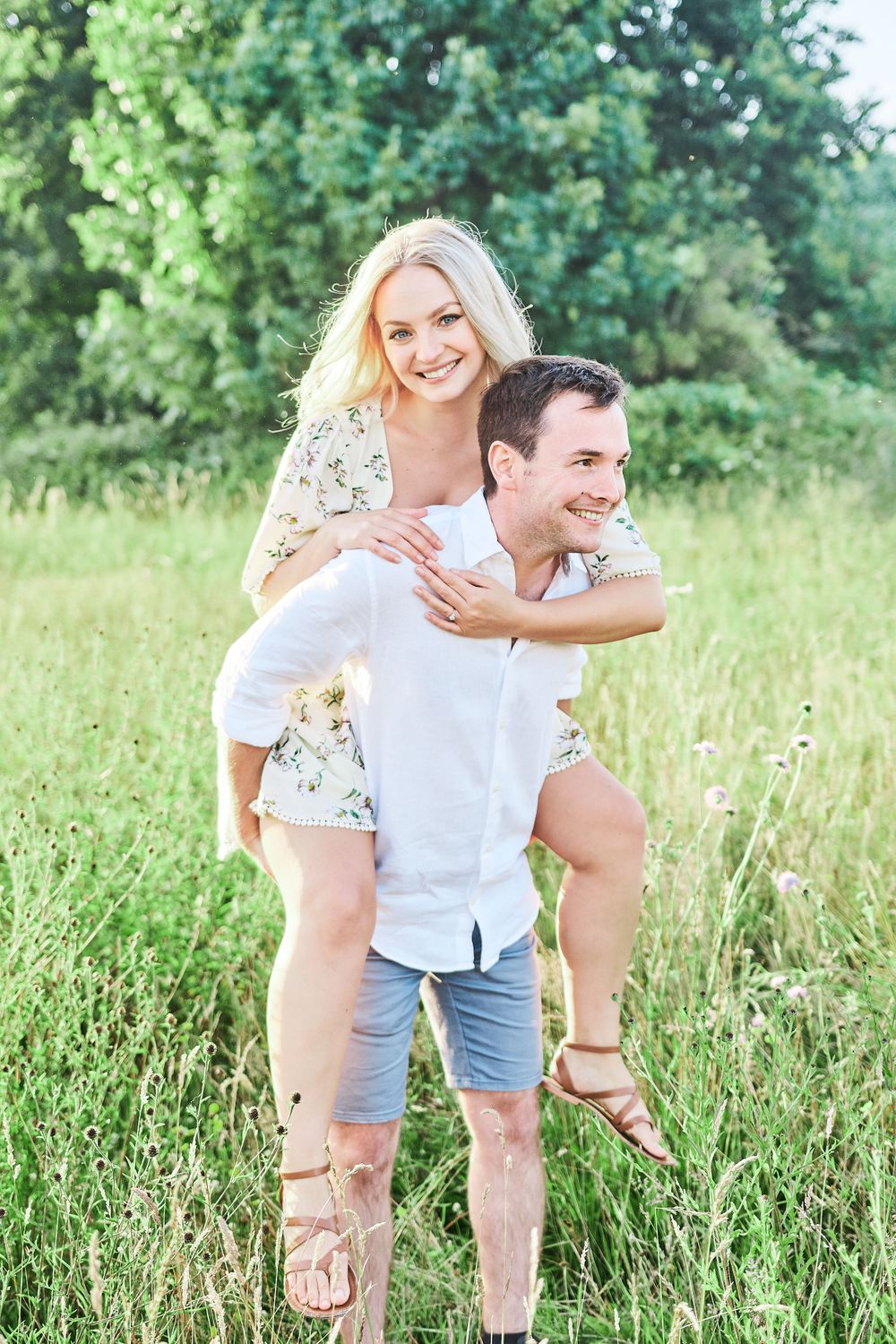 beautiful couple piggy back ride through wildflower meadow for engagement shoot at Catton Park, Norwich