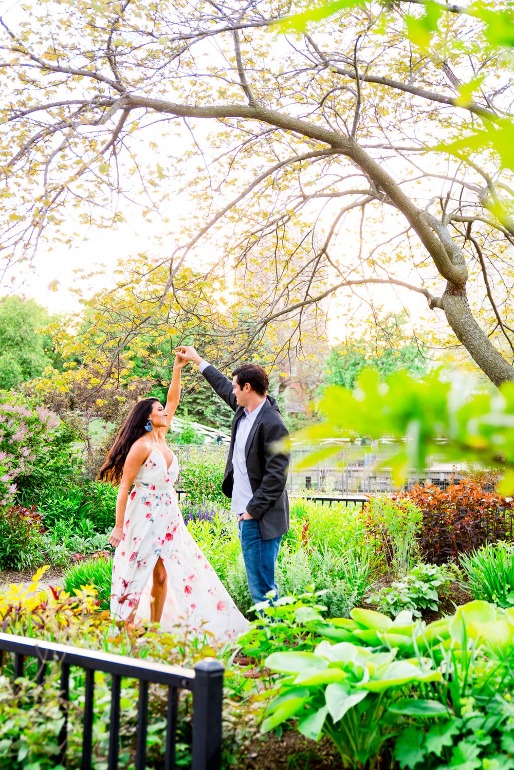 man in gray suit and jeans twirling fiance in Lincoln Park engagement pictures at sunset as she smiles