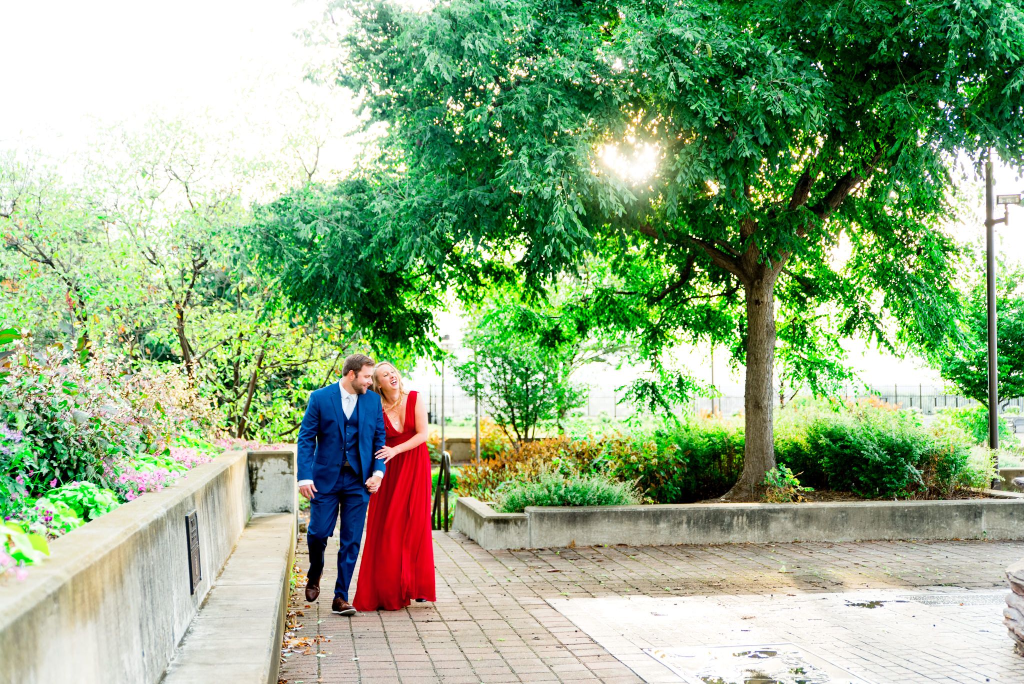 couple in red dress and navy suit walk through park at the Galt House Hotel