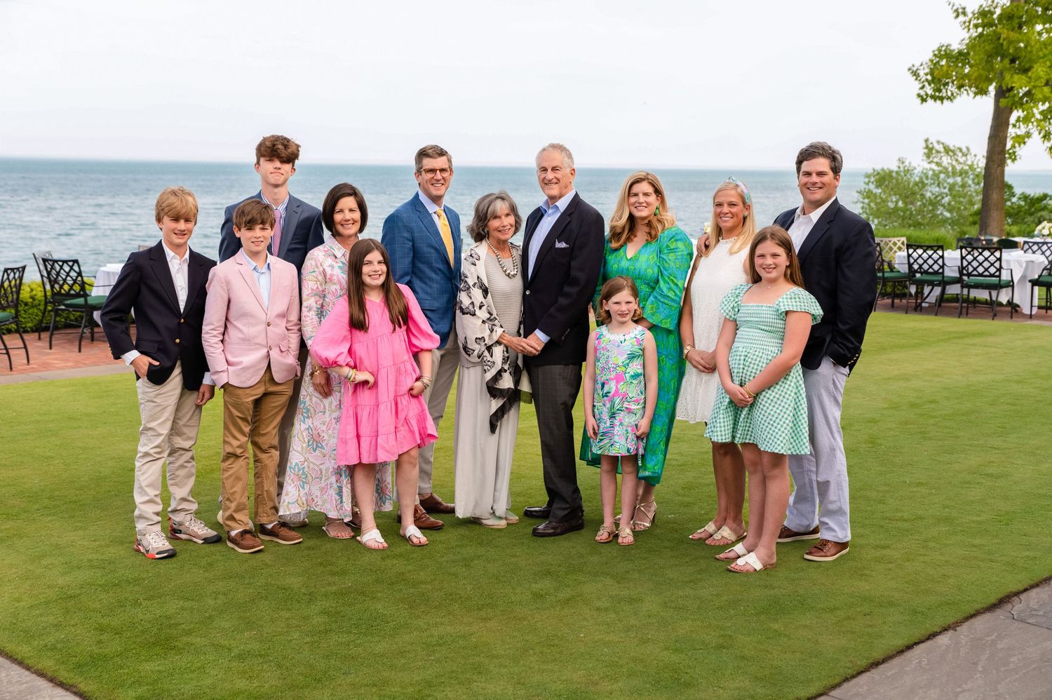 Group photo of wedding party on green lawn with ocean backdrop.