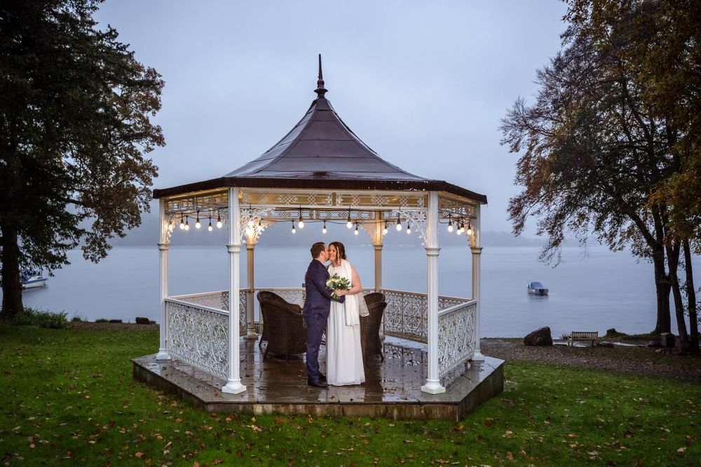Wedding couple under gazebo on lawns beside Windermere at Storrs Hall