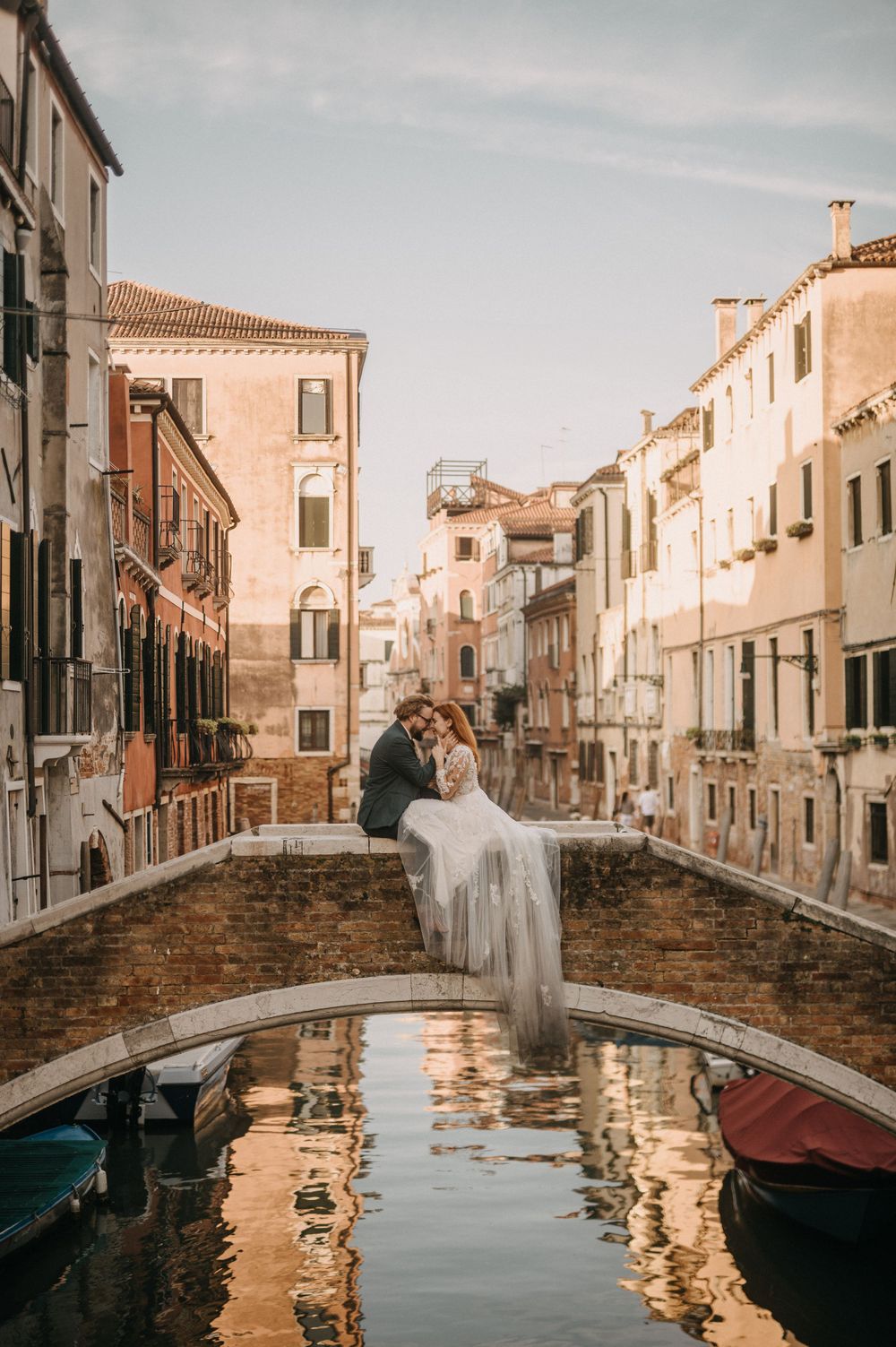 A tranquil Venice canal scene with reflections in the water and a traditional stone bridge.