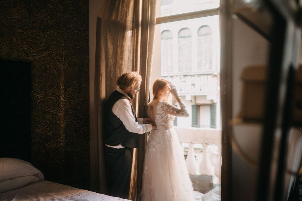 Intimate couple embraces by window in romantic boudoir photography session with dreamy natural light.