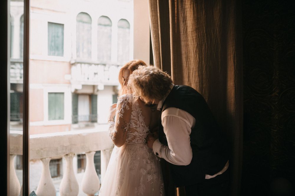 Couple embracing near window with delicate lace details and moody lighting.