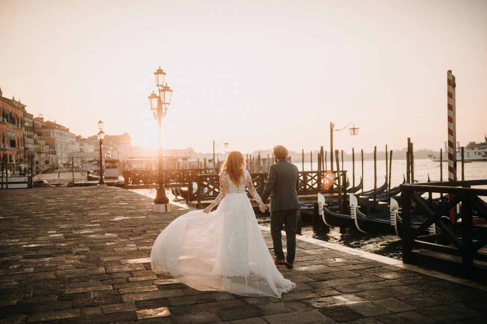 Newlyweds walk along Venice's Grand Canal as sun sets behind historic buildings and gondolas.