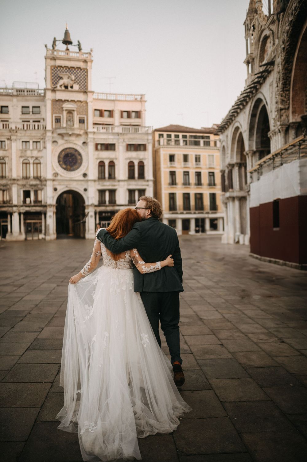 Couple in wedding attire embraces while walking through the ornate St. Mark's Square in Venice.