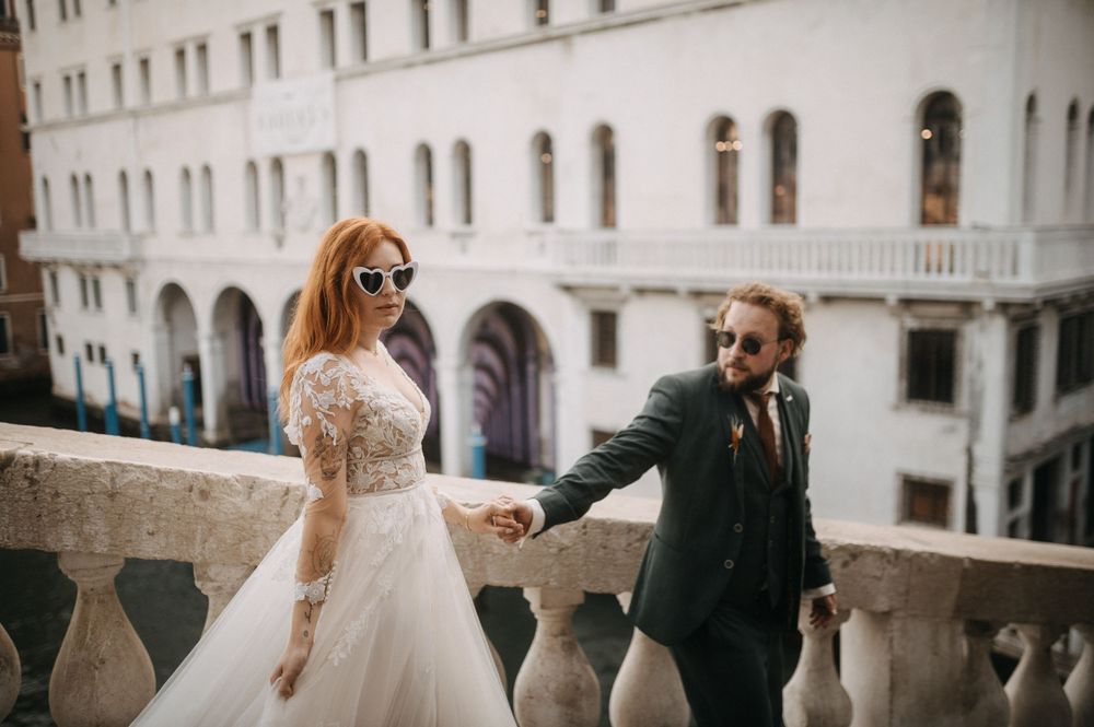 Couple in wedding attire strolls through Venice's historic streets with classic Italian architecture.