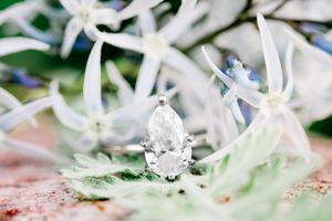 pear shaped engagement ring sitting on rock with pale blue flowers