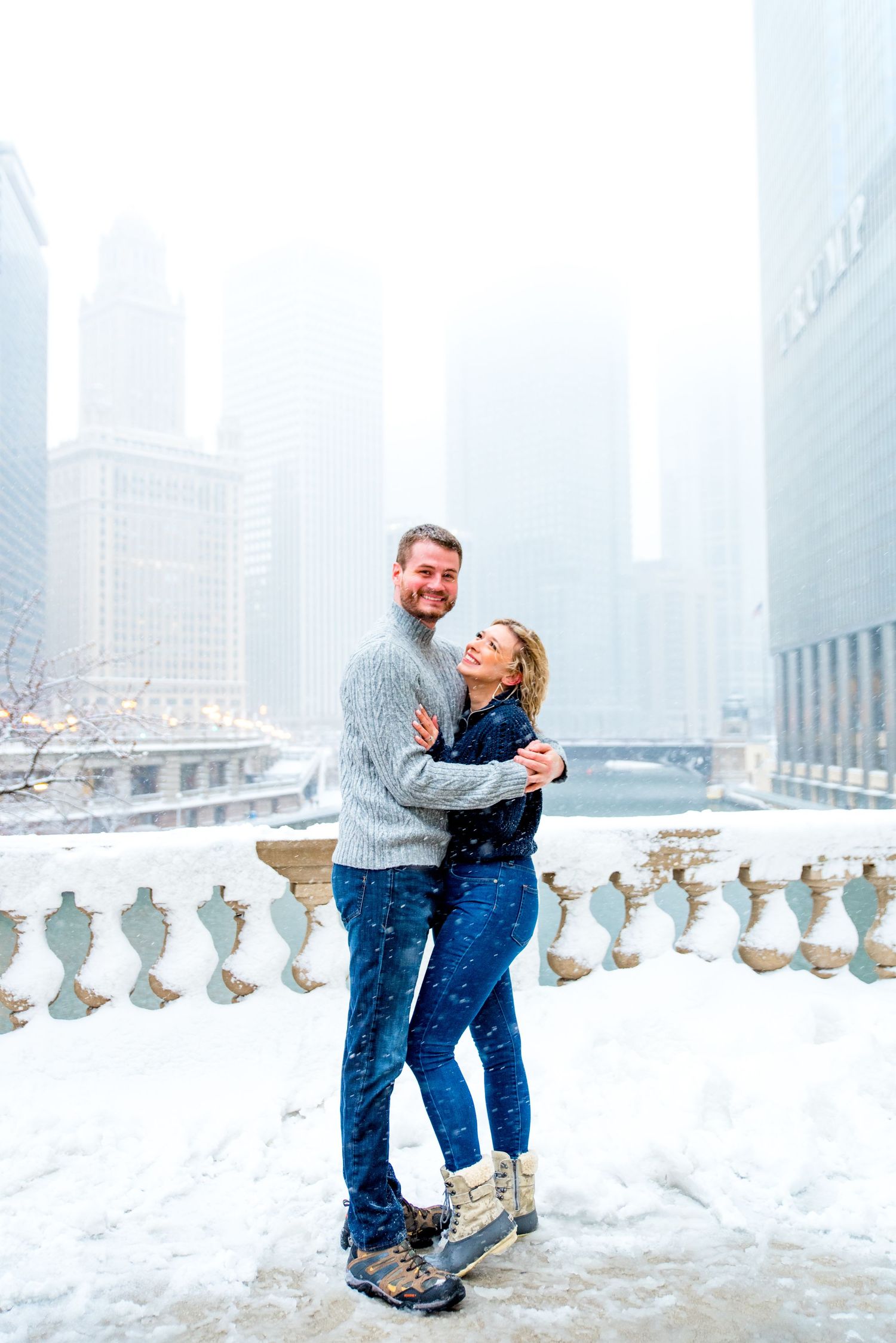 couple hugging in the snow at Wrigley Building overlooking the Chicago River for snowy winter engagement pictures