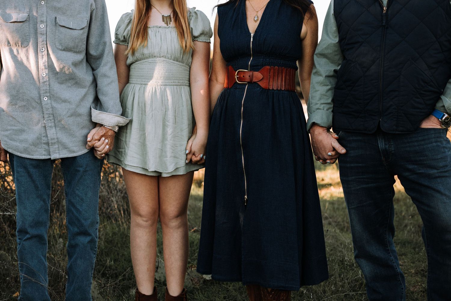 Family of four holding hands in a scenic field, showcasing a moment of love and togetherness during a family portrait session in Wimberley.