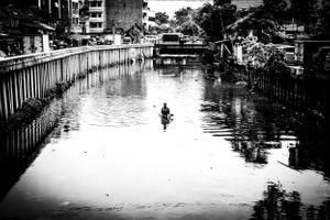 Black and white image of man collecting canal rubbish Gloodok district of Jakarta Indonesia