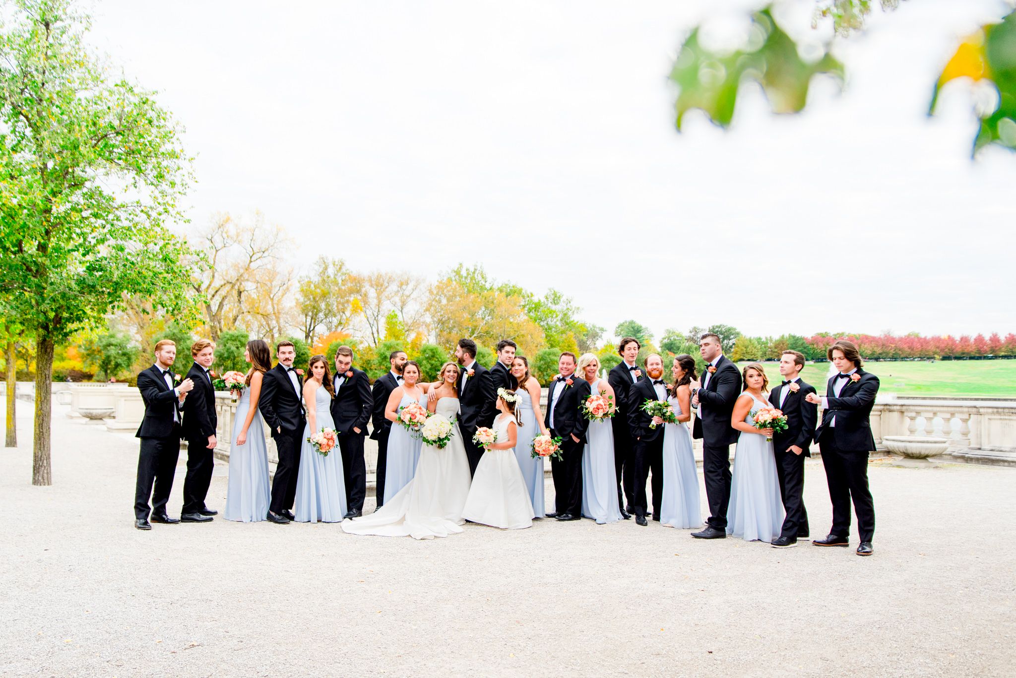 large wedding party in black suits and light blue dresses surround bride and groom at Forest Park in St. Louis