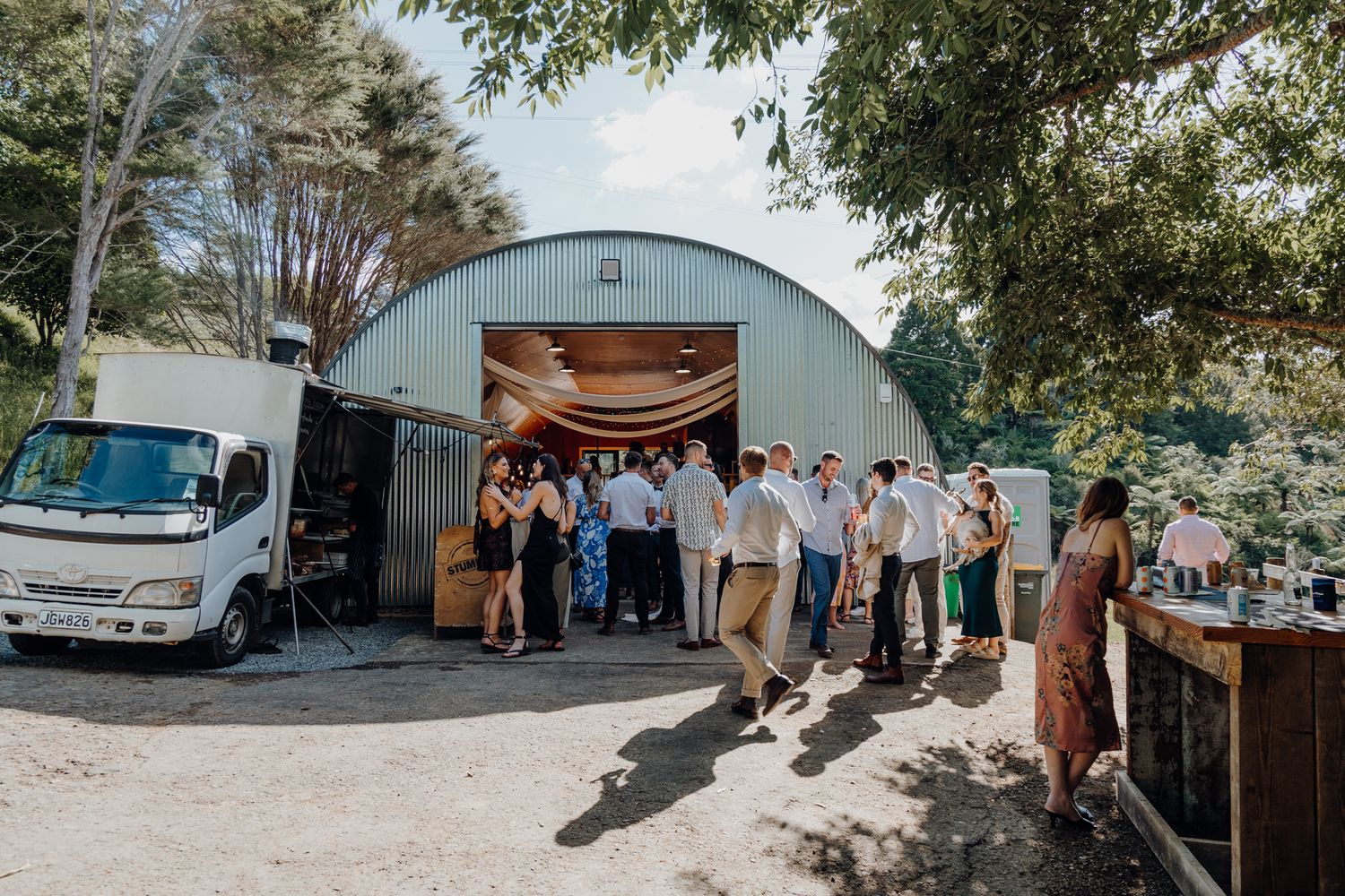 Guests gather outside a quonset hut venue for a rustic outdoor celebration.