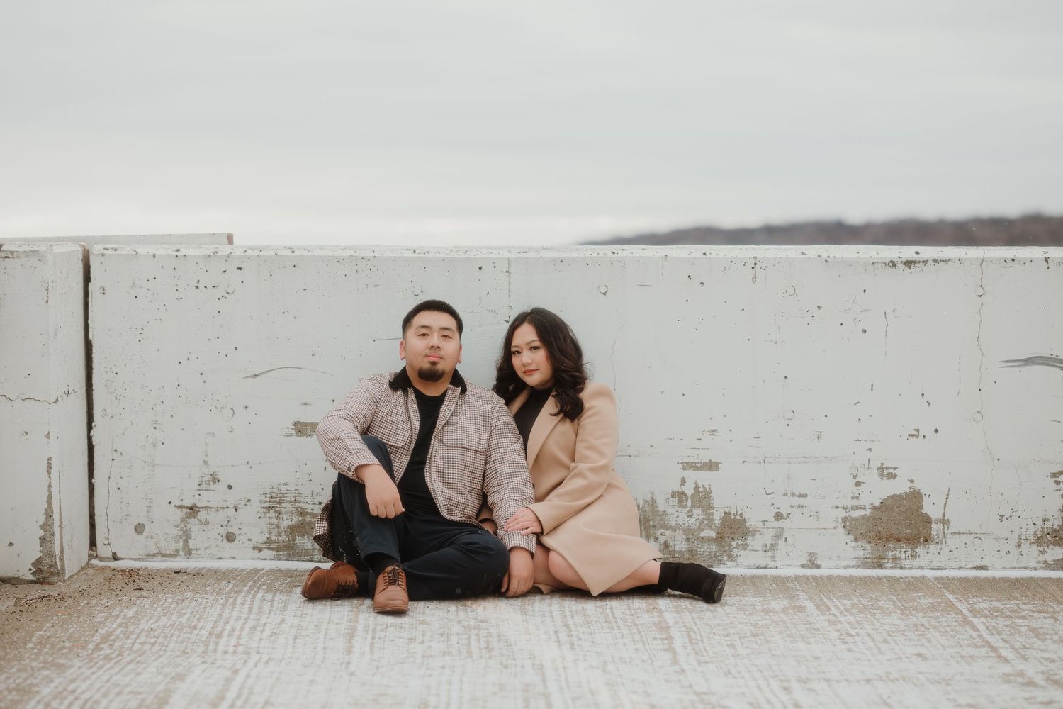 A couple sits together against a white wall in coordinated winter outfits.