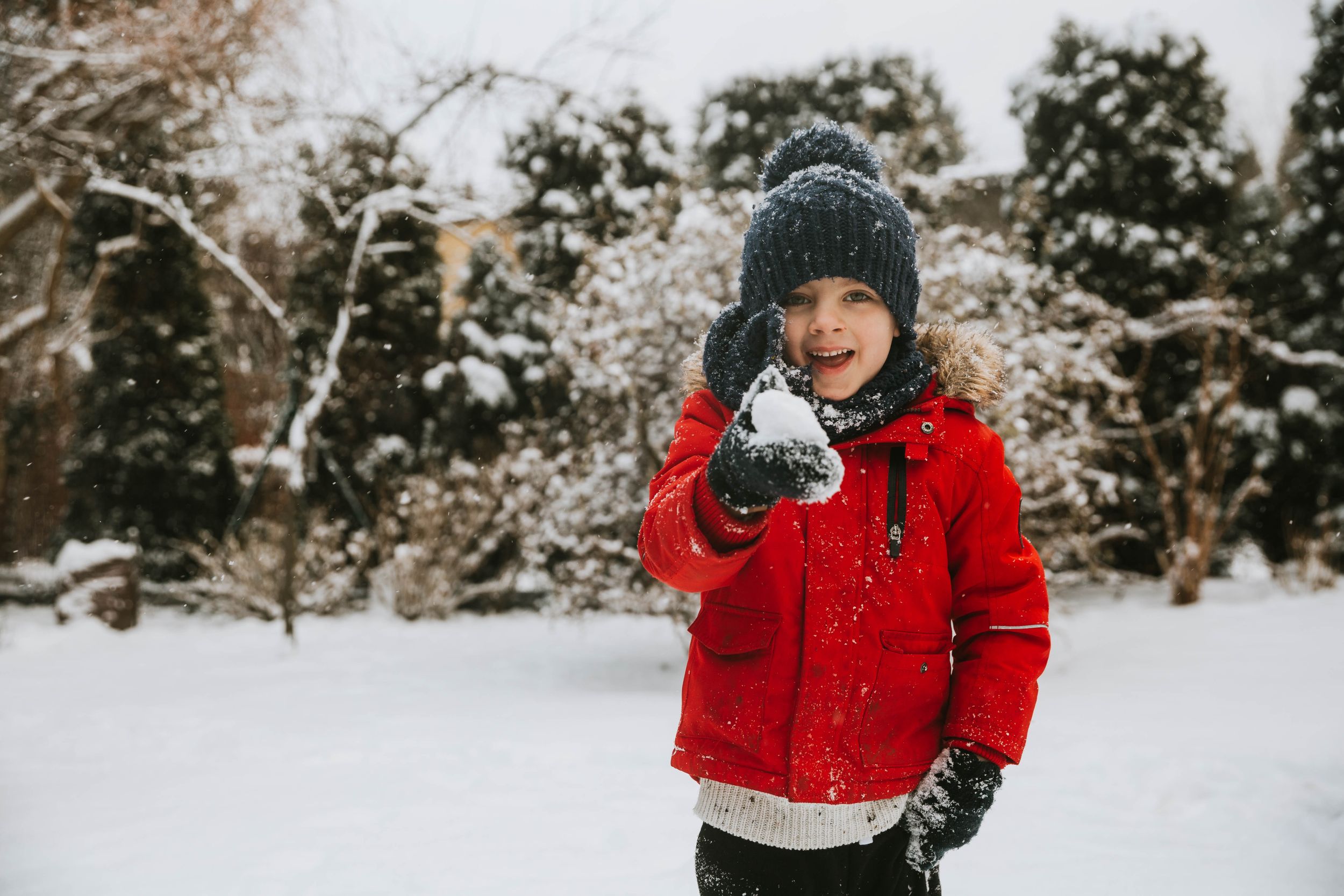 little boy holding snowball in his hands in the garden with lots of snow