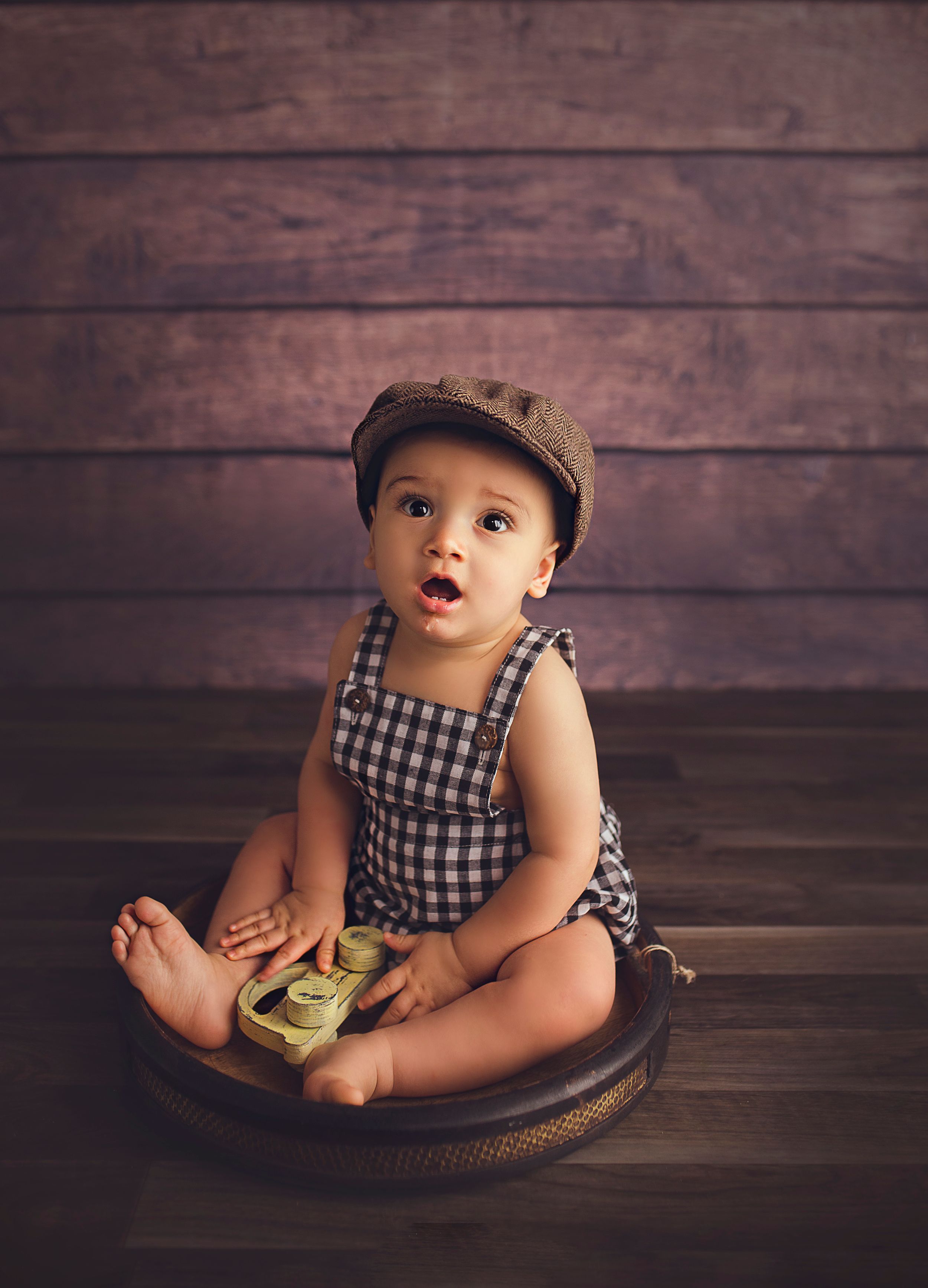 baby boy sitting on wooden bowl with vintage hat