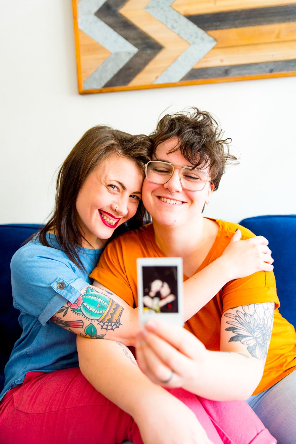 couple holding polaroid of them, in the same pose on their blue couch