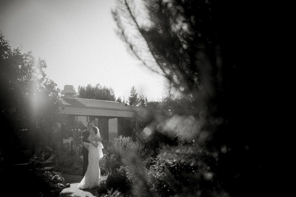 A dreamy black and white wedding photo with a hazy effect shows a couple in a garden setting at dusk.