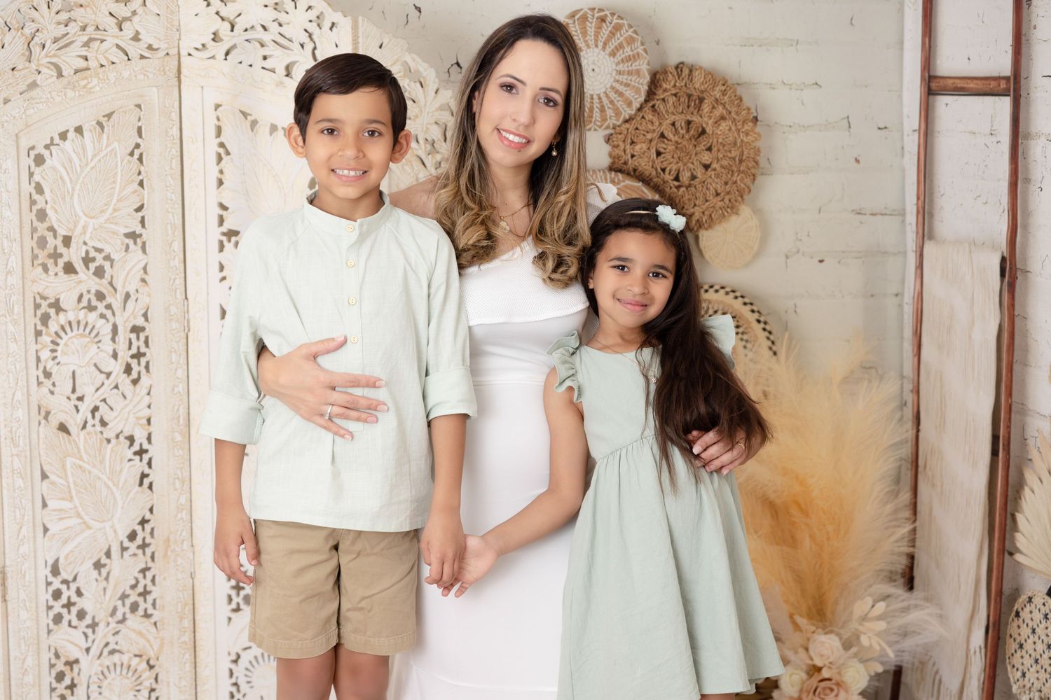 A family poses together against a white wall with decorative boho elements wearing coordinated white and mint outfits.
