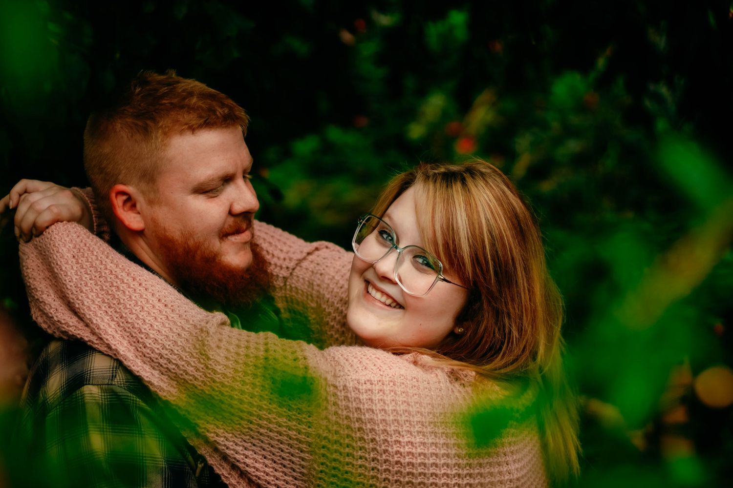 A cozy couple's portrait through leaves featuring warm autumn-toned sweaters.