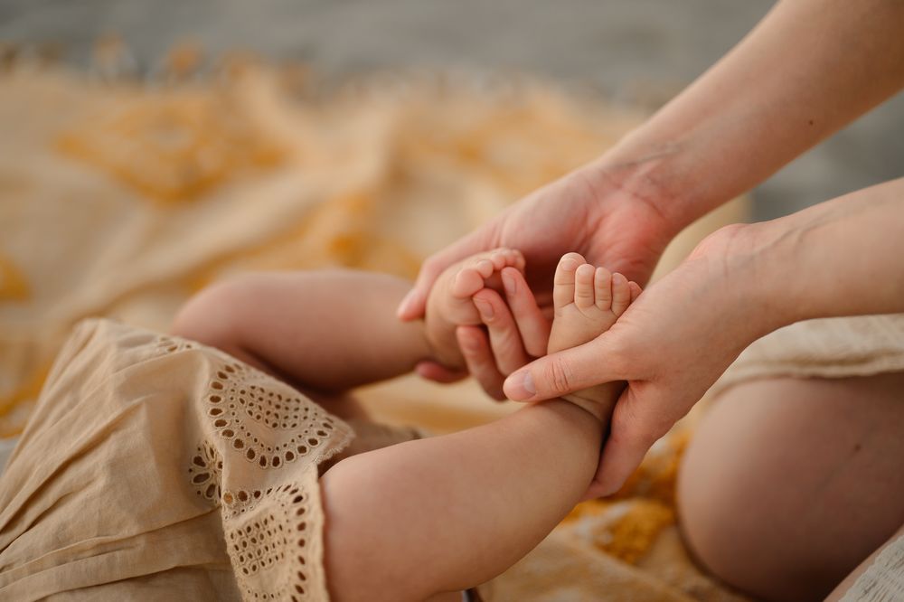 Motherhood photshoot by Tiffany Kelterer of San Diego of closeup on woman holding babies feet at Coronado beach