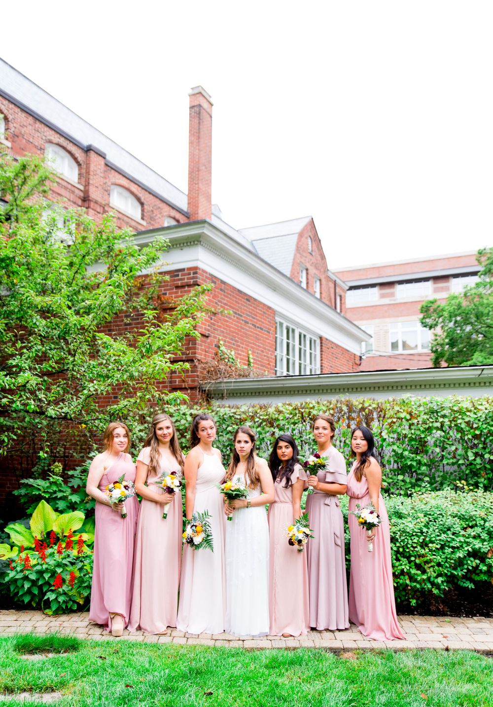 bridesmaids in pink and bride hold bouquets and give a serious face