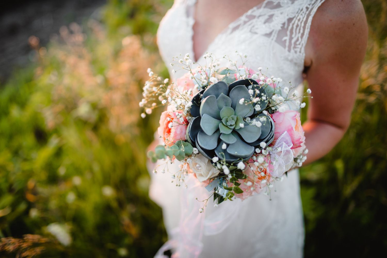 Delicate bridal bouquet featuring succulent and pink flowers against lace wedding dress.