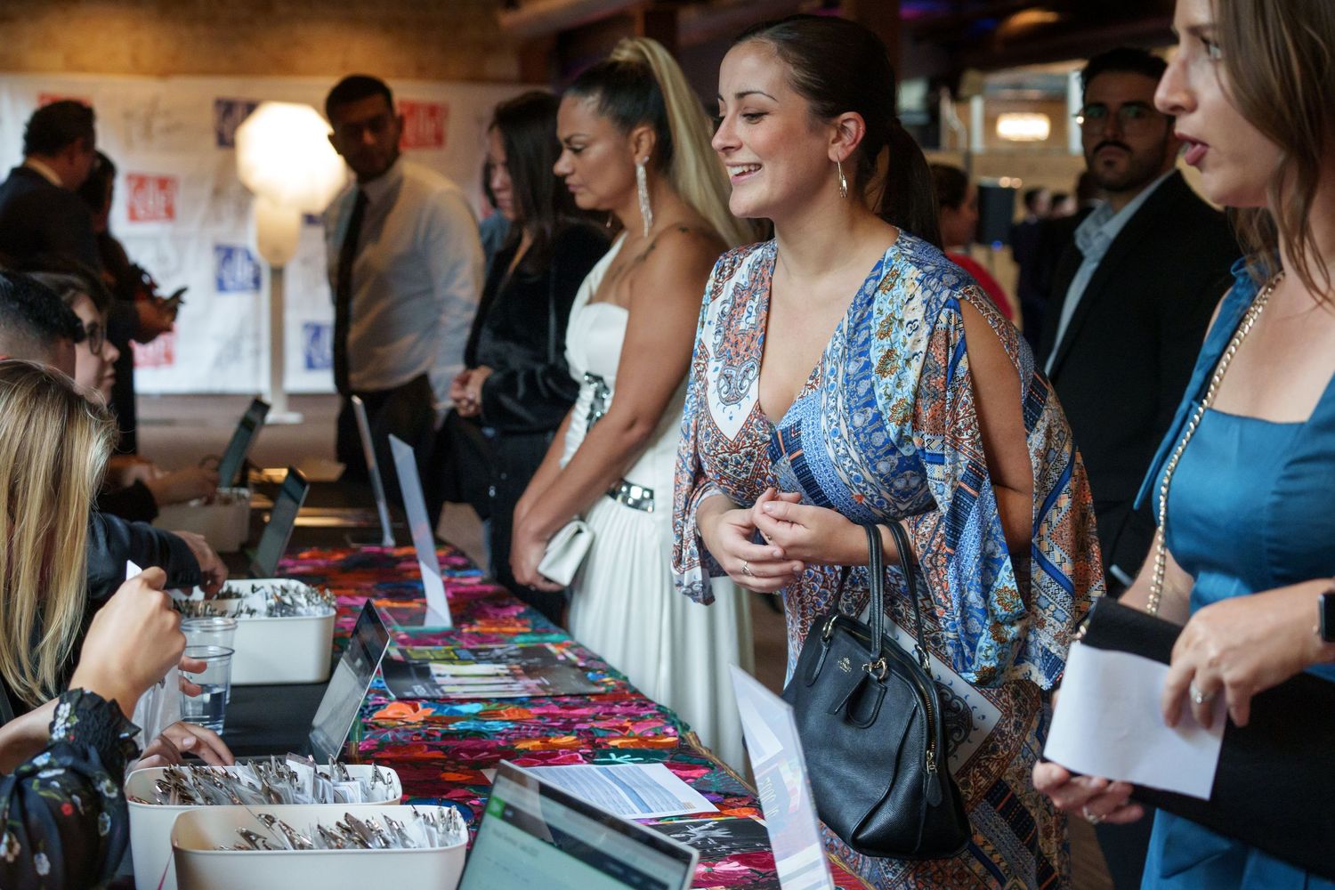 Event attendees browse merchandise displayed on a vendor table at an indoor gathering.