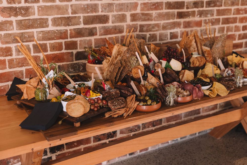 Elaborate charcuterie board display with meats, cheeses, and appetizers on wooden table against brick wall.