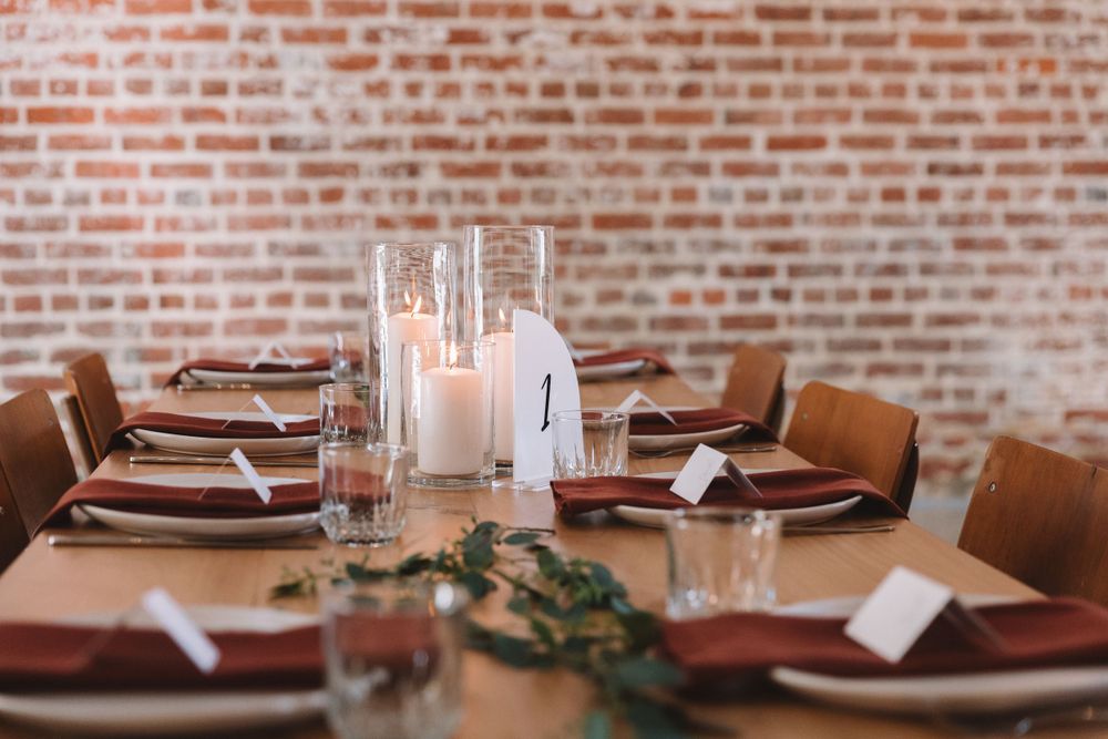 Modern rustic wedding reception table with white candles and earthy burgundy place settings.