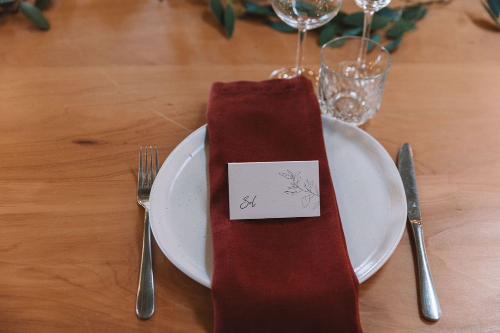 Close-up of place setting with burgundy napkin, white plate, and name card on wooden table.