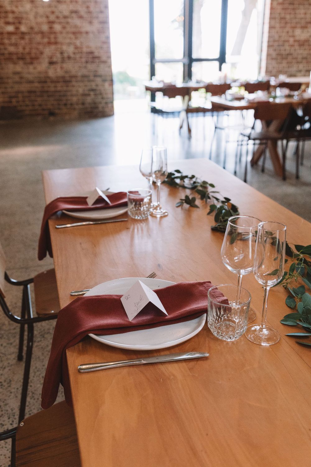 Wedding table setting with burgundy napkins and origami crane decor against brick wall.