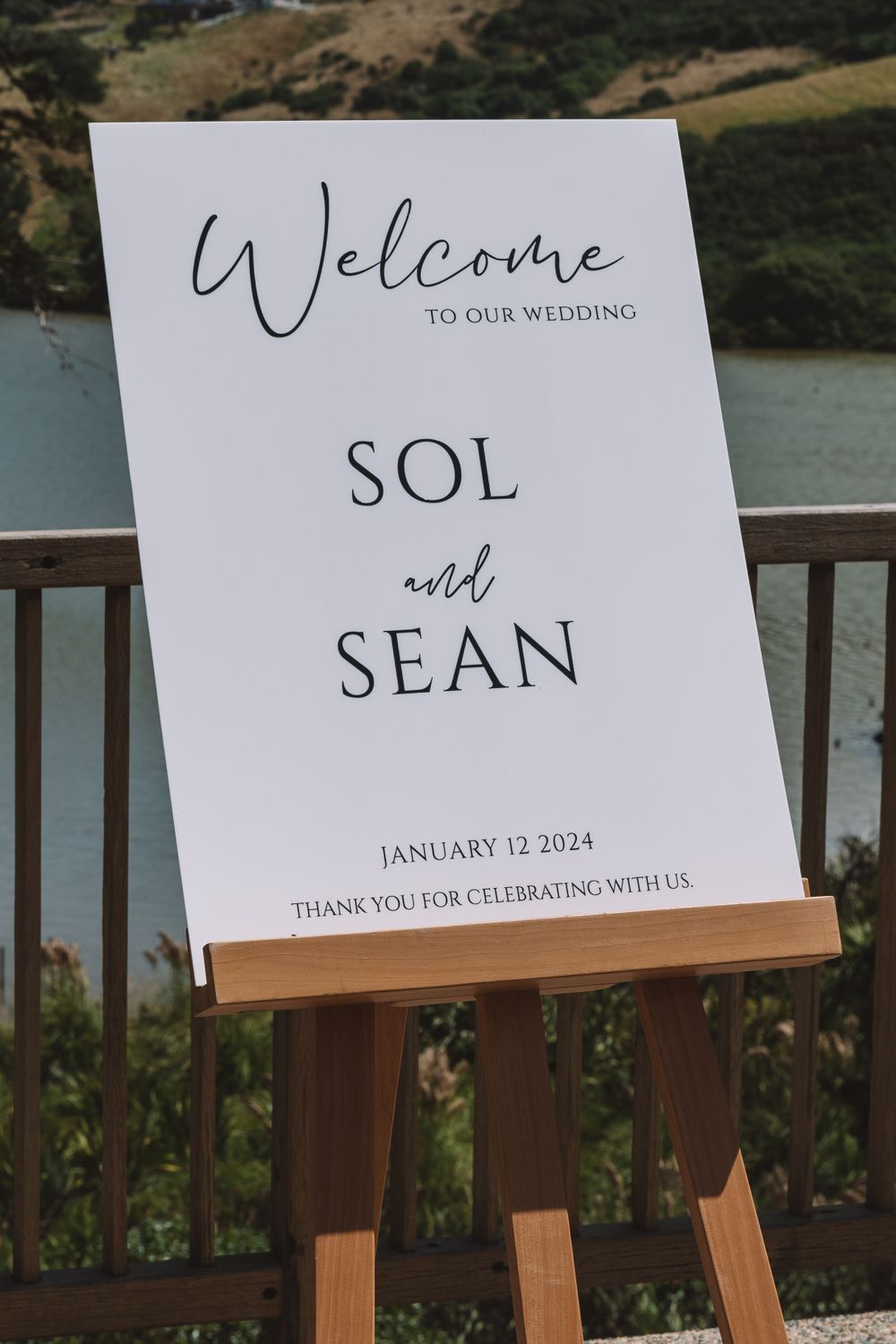 Wedding welcome sign for Sol and Sean displayed outdoors with mountain and water views in background.