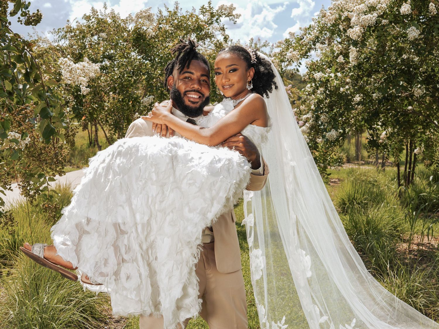 A groom carries his bride in a playful moment outdoors during their wedding photoshoot.