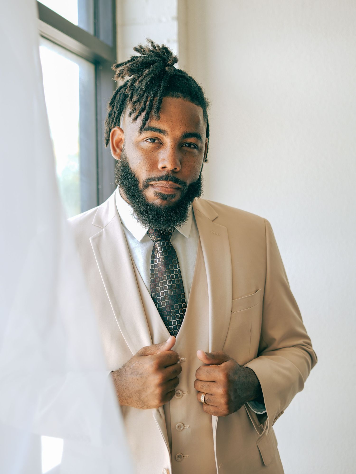 Professional portrait of man in tan suit and patterned tie near window.