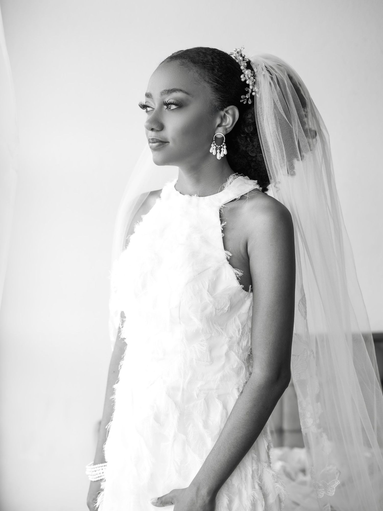 A bride in an elegant white halter wedding dress with a flowing veil poses for a black and white portrait.