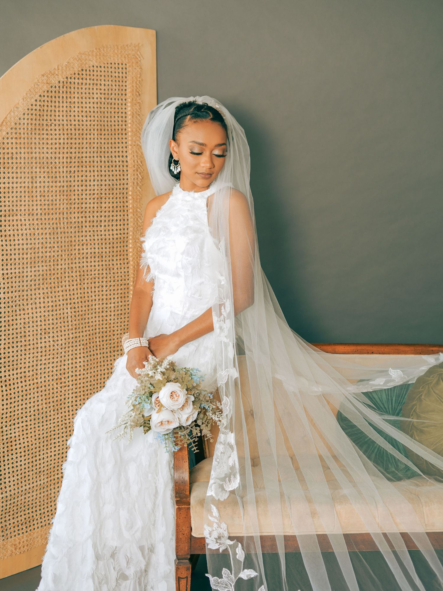 A bride poses with her bouquet in a textured white wedding gown and long flowing veil.