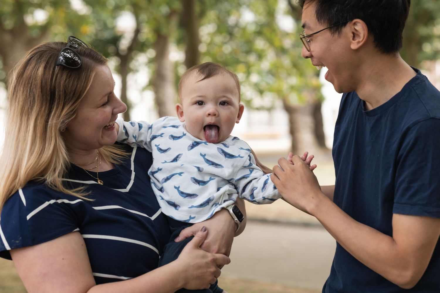 Family of three in Greenwich park. Young boy sticking out his tongue in a playful way, whilst the parents are laughing!