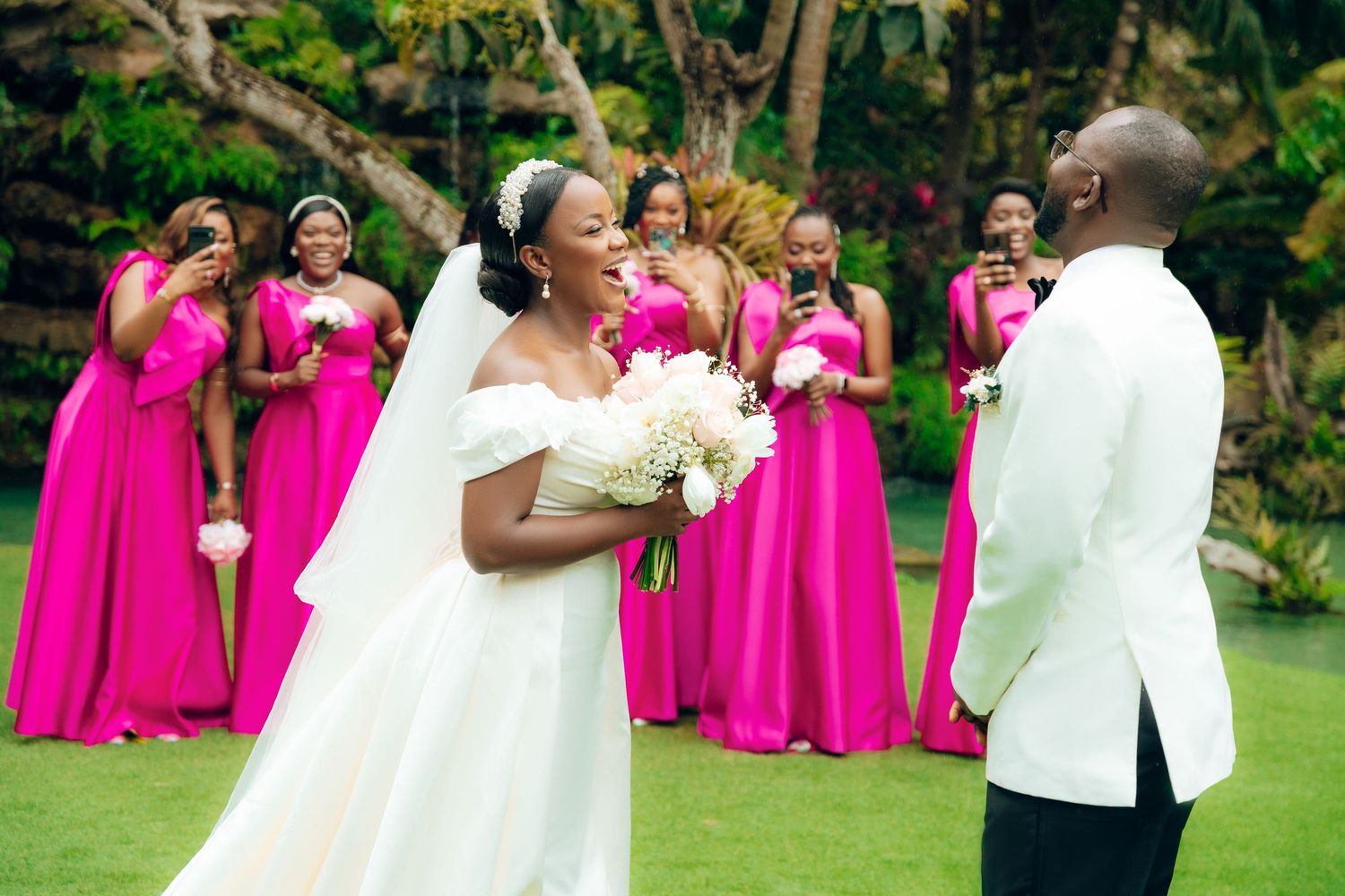 A wedding scene outdoors with bridesmaids in bright pink dresses and a bride holding white flowers.