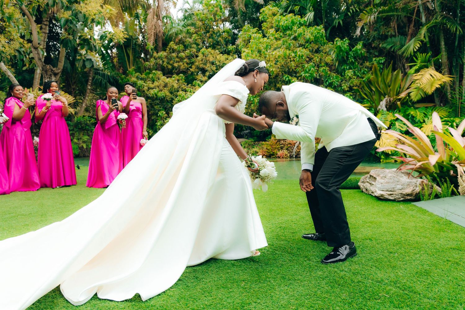 A joyful wedding celebration outdoors with pink-clad bridesmaids and a bride in a flowing white gown with long train.