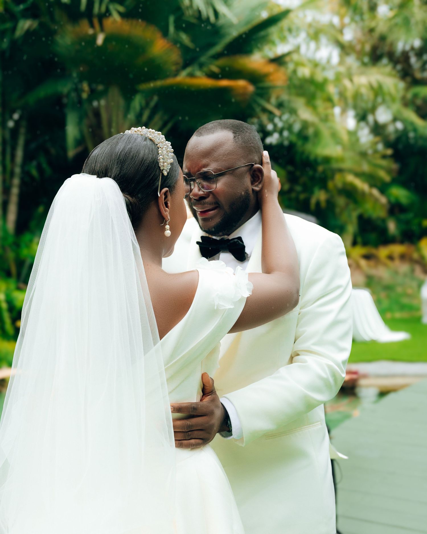 A happy couple shares a tender moment in their wedding attire against a lush tropical garden backdrop.
