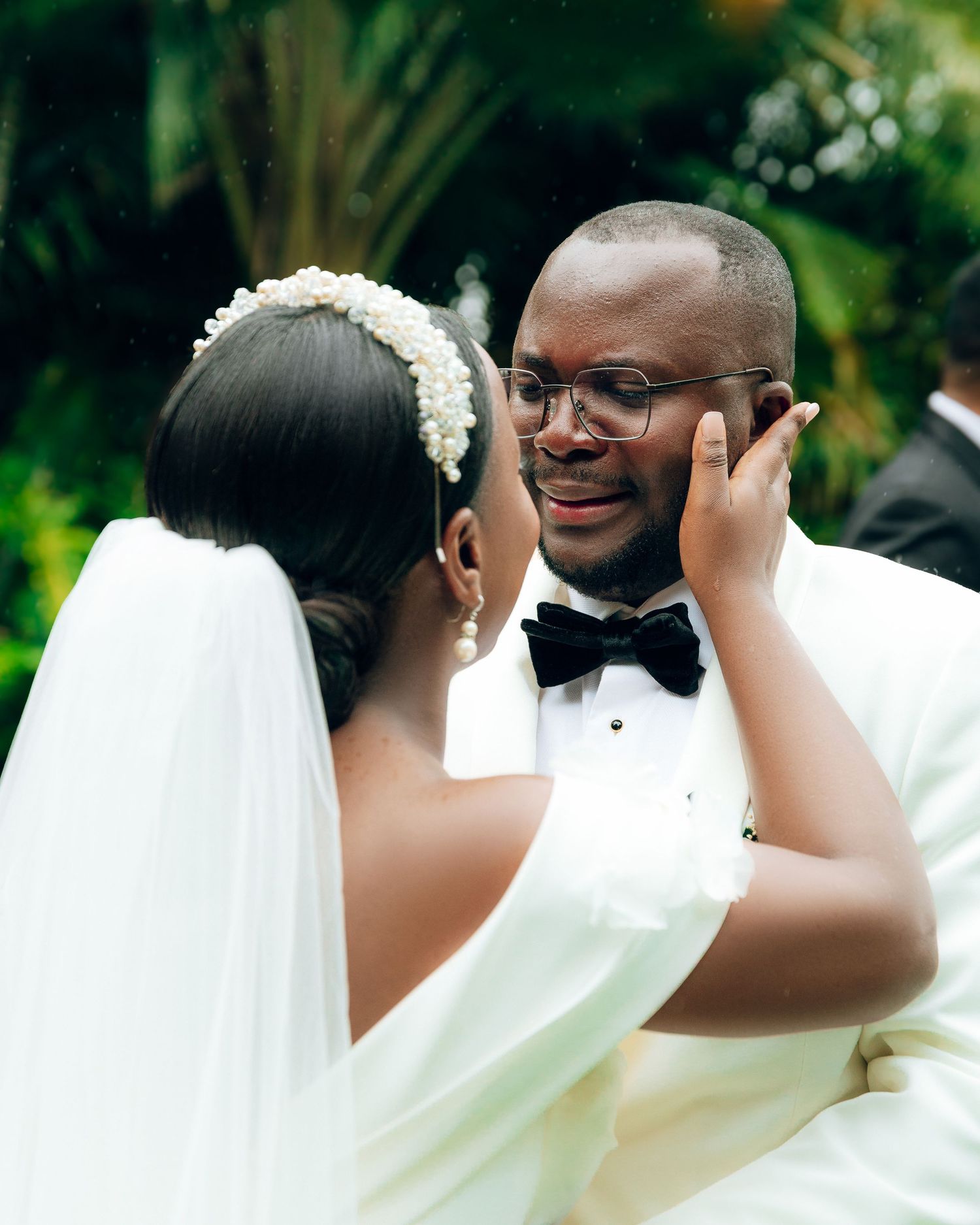 A tender moment shared between newlyweds in a garden setting with white wedding attire and formal bow tie.