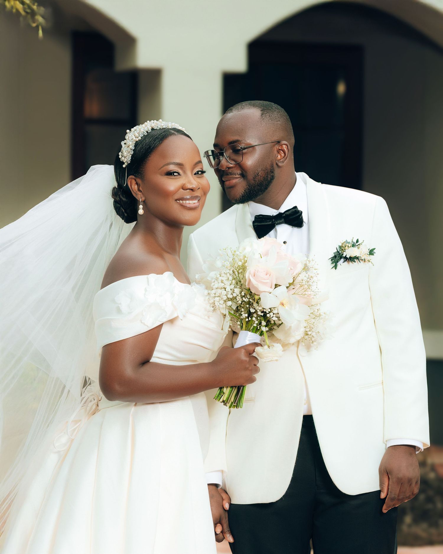 A wedding couple in white attire share an intimate moment during their outdoor portrait session.