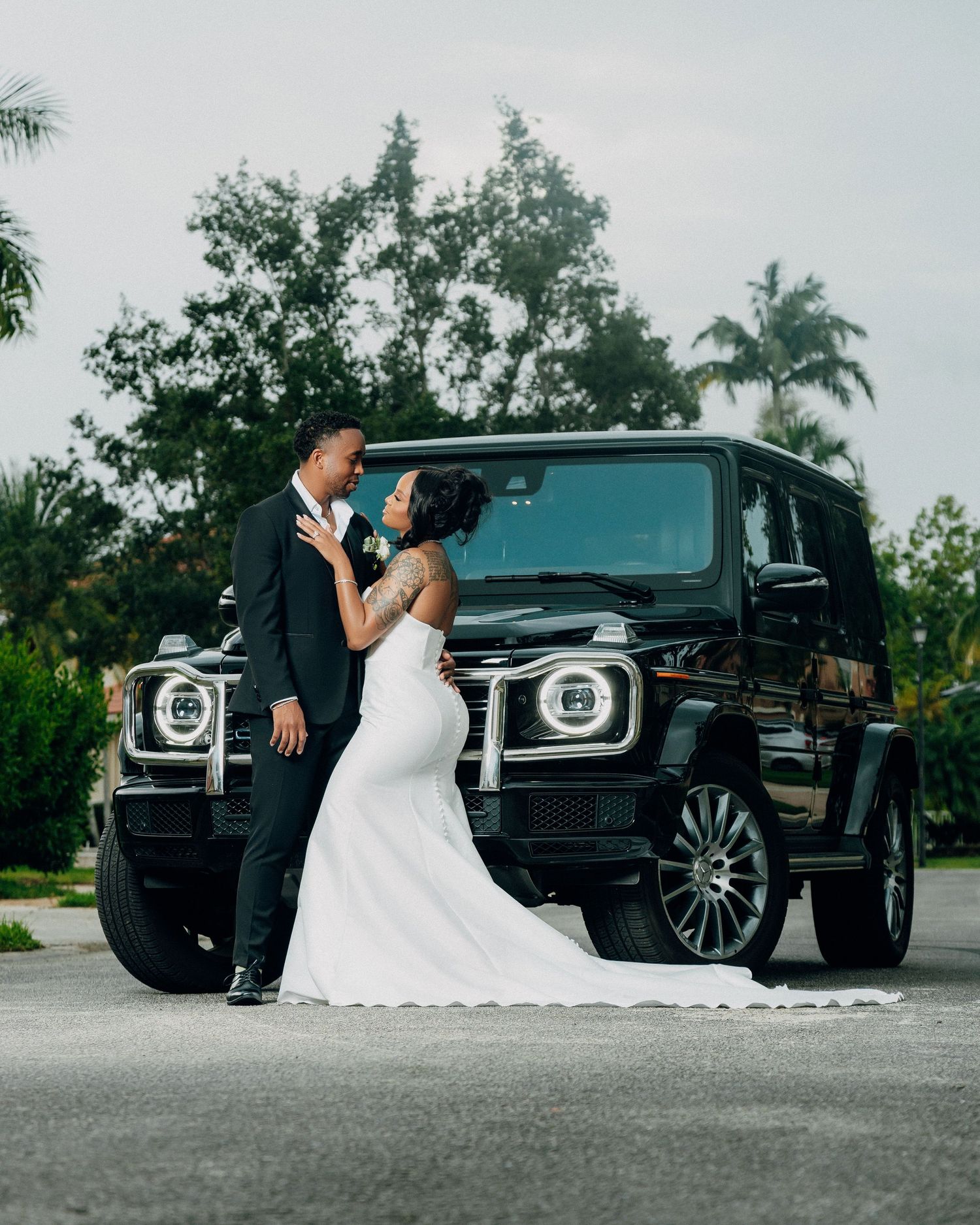 Elegant couple poses next to a black Mercedes G-Wagon on their wedding day.