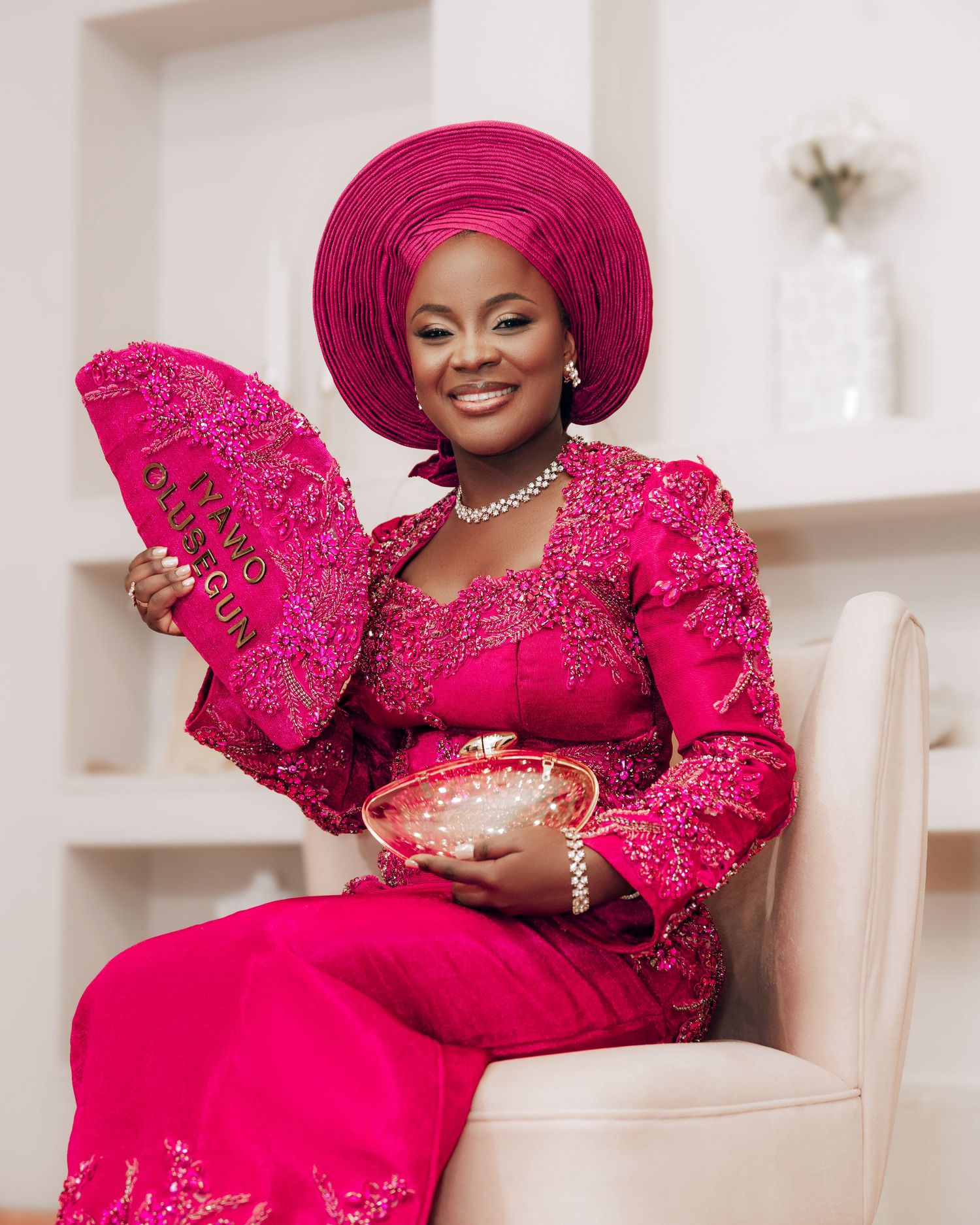 Person wearing vibrant pink traditional attire with matching headpiece poses elegantly in white interior setting.